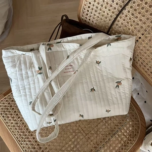 Detailed close-up of white quilted tote bag with orange fruit embroidery and French label