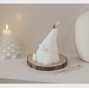 Detail of white Christmas gnome scented candle with golden bell on a wooden base
