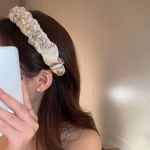 Detailed close-up of cream satin headband with pleated design and rhinestone leaf patterns