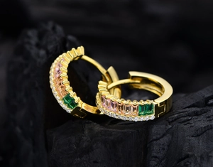 Macro detail of gold hoop earrings featuring multi-color rectangular gems and white diamonds