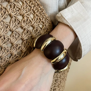 Macro shot of chunky brown acrylic and gold metal link bracelet on model's wrist