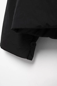 Detailaufnahme der Ärmelbündchen einer schwarzen Pufferjacke mit rundem Knopf und Stepp-Effekt