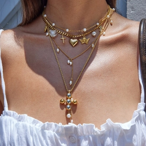 Detail of layered gold necklaces with pearl, heart, and cross pendants on model