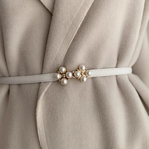 Detail of white slim leather belt with gold pearl flower buckle on a beige coat