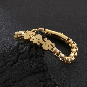 Detail of hip hop gold skull bracelet with thick woven chain on a dark stone background