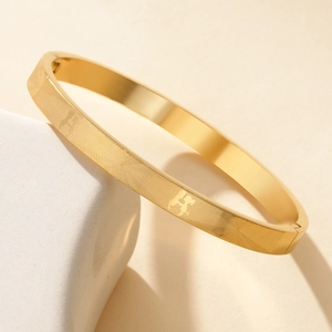 Elegante bracciale in acciaio al titanio dorato con motivo a H in rilievo e chiusura