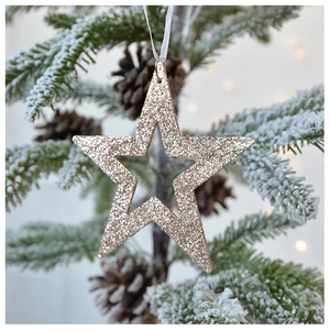 Sparkling gold star Christmas ornament hanging on a snowy pine branch with festive bokeh
