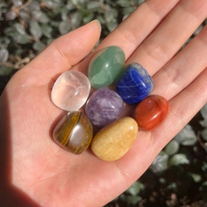 Mano sosteniendo set de siete piedras de chakra pulidas para yoga y sanación natural
