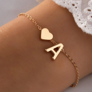 Gros plan d'un bracelet doré avec breloques cœur et lettre A porté par un mannequin