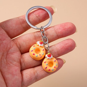 Close-up of hand holding a metal keychain with two realistic orange resin donuts and sprinkles