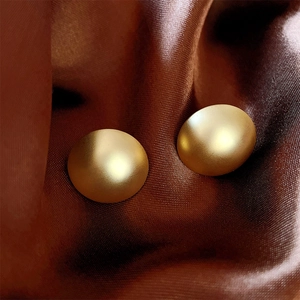 Detailed view of matte gold dome stud earrings placed on elegant dark silk fabric