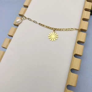 Detail of 18K gold daisy bracelet with pearl pendant on a minimalist display stand