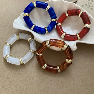 Detailed view of colorful acetate bangle bracelets with golden metal spacers in a shell tray