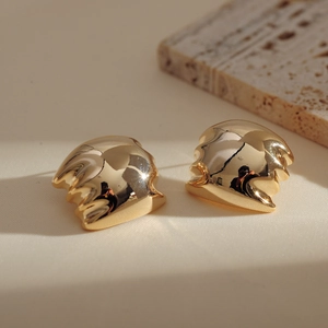 Detailed close-up of gold-plated irregular wavy earrings on elegant stone and fabric background