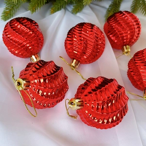 Detail von sechs roten Weihnachtskugeln mit Wellenstruktur und goldener Schnur auf Stoff
