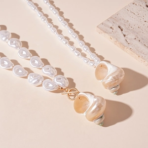 Baroque pearl and seashell pendant necklace with gold T-bar clasp on beige stone