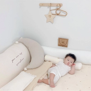 Close-up of cream cotton nursing pillow and moon-shaped cushion with soft pom-poms