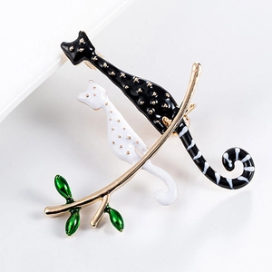Close-up of black and white enamel cat pins with gold dots on a green leafy branch