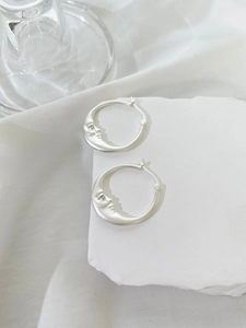 Macro detail of silver moon hoop earrings with carved face and crystal eye accent