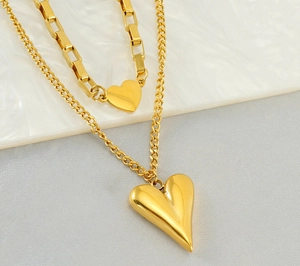Close-up of layered gold paperclip and link chain with 3D heart charms on marble