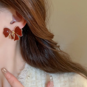 Close-up of a model wearing elegant dark red enamel bow earrings with gold-plated trim