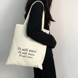 Detail der cremefarbenen Canvas-Tasche mit 'It will pass' Slogan am Modell getragen