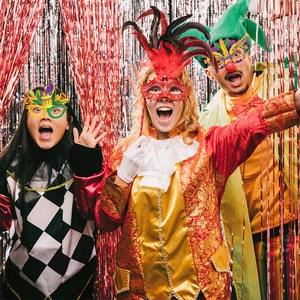 Persone con occhiali e maschere Mardi Gras in posa davanti a tende a frange metalliche