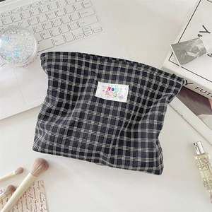Close-up of black and white plaid makeup bag with logo patch on a desk setting