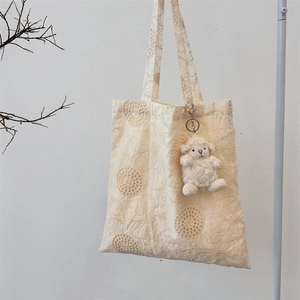 Detail of hollow lace tote bag with floral pattern and white plush sheep pendant charm