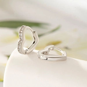 Silver heart-shaped earrings with clear cubic zirconia on a minimal nature background