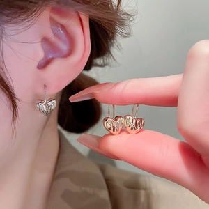 Detail of silver heart earrings featuring crinkled texture and minimalist metal design