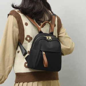 Dettaglio di un mini zaino in nylon nero con finiture in pelle marrone su modella