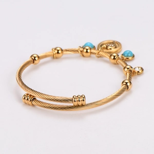 Detail of golden twisted rope bracelet featuring sky blue beads and a round pendant charm