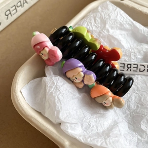 Détail de la pince à cheveux noire avec quatre poupées 3D colorées sur papier texturé