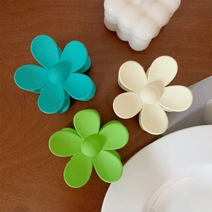 Detail of matte flower hair claws in teal, beige, and lime green on dark wood background