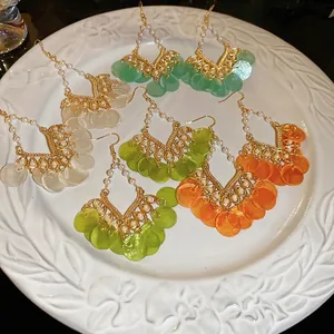 Bohemian round shell pearl tassel drop earrings in four colors on a white ceramic display plate