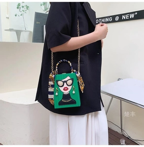 Detail of green box evening bag with cartoon print, gold chain, and floral silk scarf