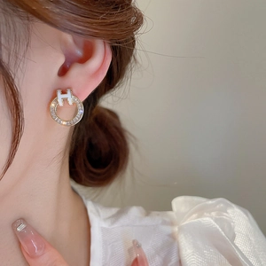 Close-up of gold-plated hoop earring with clear zircons and white enamel H logo