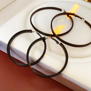 Détail de quatre boucles d'oreilles créoles en cuir noir de deux tailles sur socle