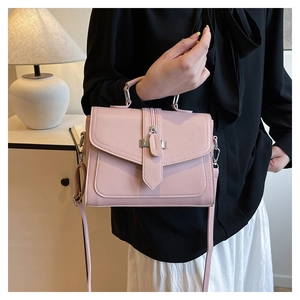 Close-up of pink square handbag with premium hardware and flap closure held by model