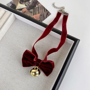 Détail d'un choker en velours bordeaux avec nœud et cloche dorée dans son écrin