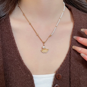 Detailed close-up of gold-plated ginkgo leaf pendant with pearls on a necklace