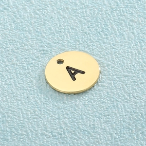Macro shot of gold stainless steel circular pendant with cut-out letter A on blue surface