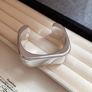 Close-up of a wide polished silver wave open bangle placed on a cream velvet jewelry box