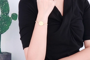 Detail of double-layer gold stainless steel bracelet with pearls and sunburst charm