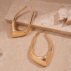 Détail de boucles d'oreilles géométriques dorées sur un socle en pierre naturelle