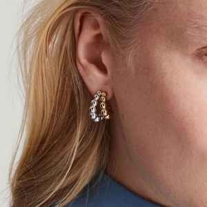 Modern dual-tone gold and silver beaded C-shaped hoop earrings worn by a model