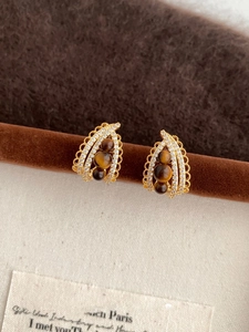 Detailed macro view of gold-tone teardrop earrings with brown beads and zircon inlay