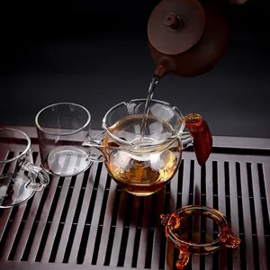 Heat-resistant glass tea pitcher with wooden handle and matching strainer set on wooden tray