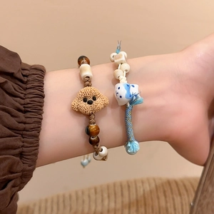 Close-up of handmade ceramic teddy dog and lucky cat charms on woven cord bracelets